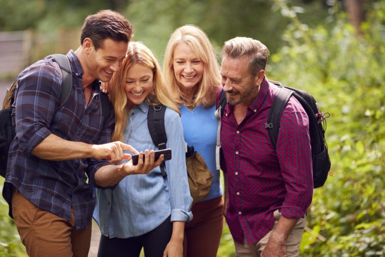 Group Of Friends Hiking In Countryside Looking At Picture On Phone As They Hike Along Path